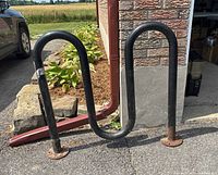 Full view of the black metal 3-loop wave style bike rack against an outdoor background showing the overall shape and condition.