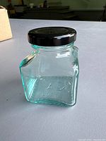 Front view of one square glass jar with black lid on tabletop