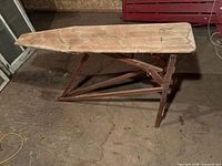 Side view of antique wooden ironing board showing the top surface and angled support legs.