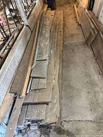 Stacked assorted rough cut wood planks and boards on ground, showing varying sizes and rough edges