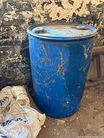 Blue plastic barrel placed on the dirt floor against a stone wall, showing general condition and overall height.