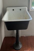 Cast iron utility sink front view showing white enamel interior and black exterior on pedestal under sink.