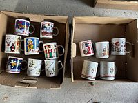 Top view of two boxes containing 13 assorted Christmas-themed mugs with various prints such as Santa, snowmen, reindeer, and nutcracker soldiers.