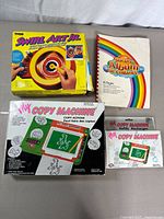 Photo of all three items together showing Tyco Swirl Art Jr. box, My Copy Machine box and refill pack, and Sticker Album Book.