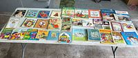 Wide view of all 32 assorted vintage kids books laid out on a table, showing colorful covers and various titles.