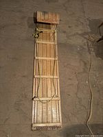 Top-down view of entire wooden toboggan showing its length and construction from multiple wooden slats with rope bindings on sides.
