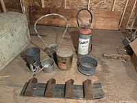 Wide shot showing all items including maple syrup can, aluminum pot, sprayer, woven basket, metal bucket and grain elevator belt chunk with mounting brackets.