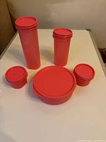 Photo showing five pink Tupperware containers of different sizes on a table: two small round, one large round, and two rectangular tall containers