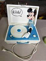 Full view of the open record player with Mickey Mouse graphic inside lid and record player visible in base.