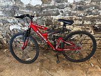Red Supercycle Nitrous 2G mountain bike leaning against a stone wall, showing full side profile.