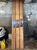 Three sealed packs of Heritage Pine mini pickwick paneling leaning against a wall in a basement or storage area.
