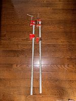 Two metal pipe clamps laid on a wood floor, showing full length and red clamp handles and jaws.