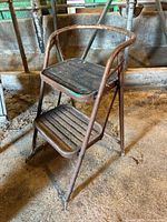 Front and side view of a vintage two-step metal stool showing rust and wear.