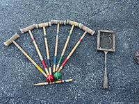 Six wooden croquet mallets arranged fan-like showing the colors on the handles and two croquet balls in front.