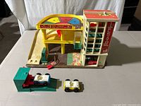 Full view of the vintage Fisher Price Little People #930 Parking Ramp Service Center Garage playset with two cars and the green service ramp with red lever in front.