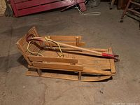 Side view of vintage wooden kids sleigh with attached handle and rope pull, showing wooden runners with metal bars.
