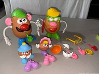 Mr. and Mrs. Potato Head figures standing with kid potato figures and various accessories laid next to them.