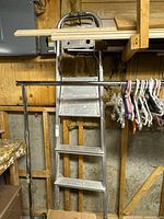 Full view of 6 foot folding metal step ladder showing five steps, top handle, and folded position against wooden wall.