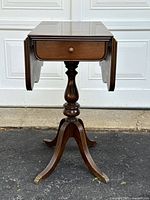 Full view of antique walnut drop leaf side table with leaves down, showing single drawer and pedestal base with clawfoot legs.