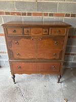 Front view of antique walnut dresser showing six drawers with bookmatched veneer and metal ring-pull handles.