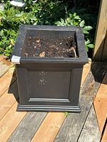 Front view of the black plastic square planter showing its paneled design and soil inside.
