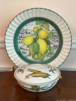 Front view of the Ceramica Due Torri serving dish featuring yellow lemons and green leaves, scalloped green rim, and the Royal Worcester Evesham casserole dish with matching vegetable motifs placed in front.
