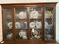 View of the entire china cabinet showing all shelves filled with floral dishes, crystal glassware, and silver items.
