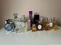 Overview of seventeen perfume bottles on tabletop against neutral wall