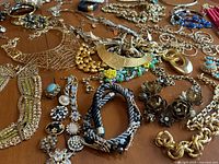 Top-down view of the assorted gold-tone costume jewelry spread on a flat surface, showing various necklaces, bracelets, and earrings including gold chains, rhinestones, and fabric accents.