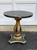 Front angled view of the vintage Italian pedestal side table showing the round black marble top with gold and gray veining, and the detailed wooden base with gold and black paint.