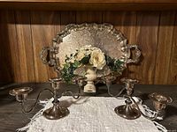 Photo showing the large ornate silver tray behind the pair of triple candelabras with a floral decoration inside the tray
