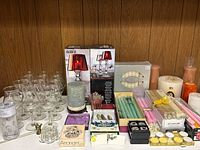 Full view of lot with glasses, boxed candles, candle holders, taper candles, tealights, and wine glass charms.