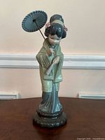 Front view of the figurine showing the geisha holding the fan and parasol, displaying the detailed kimono and hair decoration.