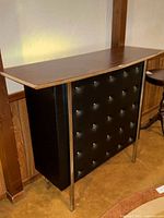 Full front view showing the tufted black vinyl panel with chrome buttons and chrome legs beneath faux rosewood top