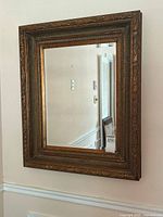 Full frontal view of the rectangular antique style mirror hanging on a wall showing ornate gold gilt wooden frame and reflective glass surface.