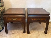 Front view of the pair of Asian style wood side tables placed side by side on carpet.