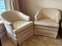 Pair of vintage blush pink barrel back club chairs with floral jacquard upholstery shown angled side view.