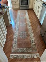 Full length view of the pink and beige floral runner rug laid in kitchen. Shows overall pattern and condition including visible staining.