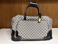 Front view of Ralph Lauren rolling duffel bag with monogram pattern and leather-trimmed handles on a white surface against wooden background.