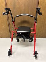 Front view of the red rollator walker showing ergonomic hand brakes, padded backrest, and four wheels.