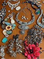 Various silver-tone and colorful costume jewelry pieces laid out on a wooden surface, showing necklaces, earrings, brooches, and pendants.