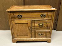 Front view of small vintage wooden washstand showing door, drawers with metal handles, and wear on surface.