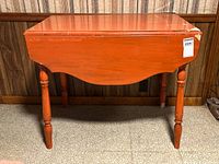 Front view of the vintage orange drop leaf table with one leaf down.
