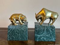 Front view of both brass bull and bear bookends on green marble bases
