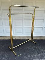 Full view of brass tone metal clothing rack showing overall structure, T-shaped base, vertical ridged supports and horizontal hanging bars.