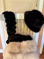 Two fox fur collars, one beige and one black, displayed on a chair alongside a black fox fur hat.