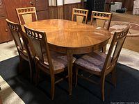 Full view of wooden oval extendable dining table with 6 matching chairs around it, showing wood grain and chair design details.
