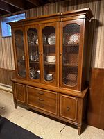 Full view of vintage solid wood china cabinet with glass doors showing plates inside.