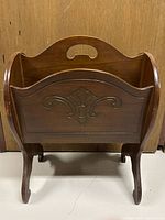 Front view of vintage walnut magazine stand showing carved front panel, curved legs, and top handle cutouts.