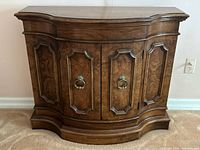 Front view of the vintage wood console cabinet showing carved panel doors and brass hardware.
